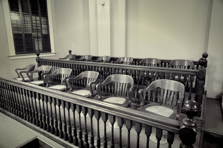 Empty jury box in a courtroom, rows of wooden chairs behind a railing