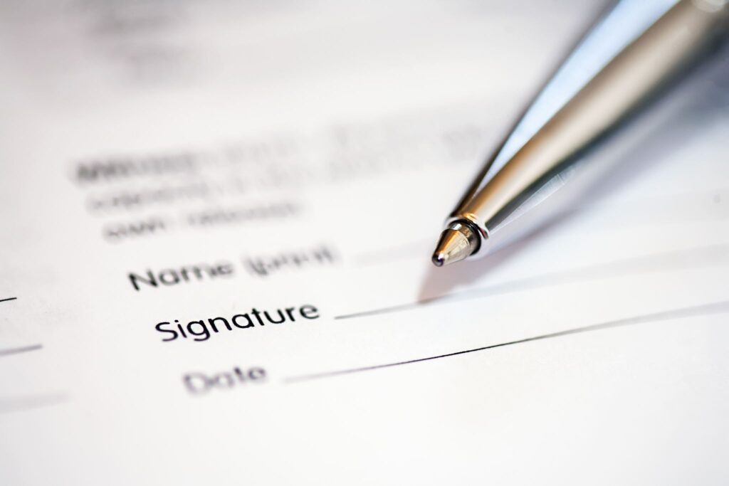Pen resting above the signature line of a printed form